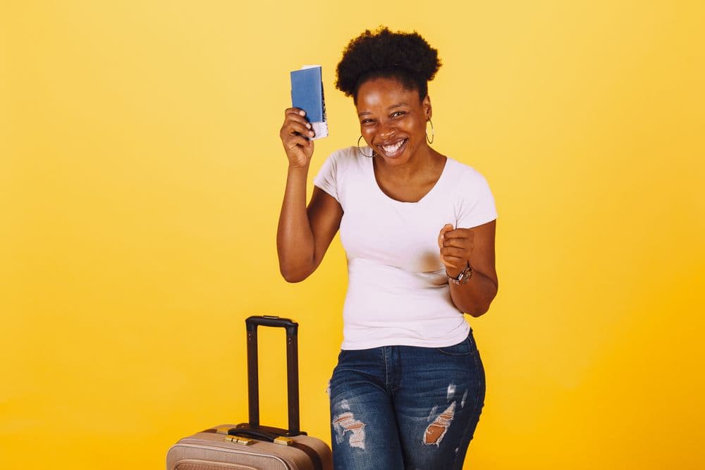 A smiling traveller holding a passport, with a suitcase